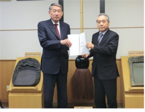 二人で紙を持って立っているスーツ姿の男性の写真