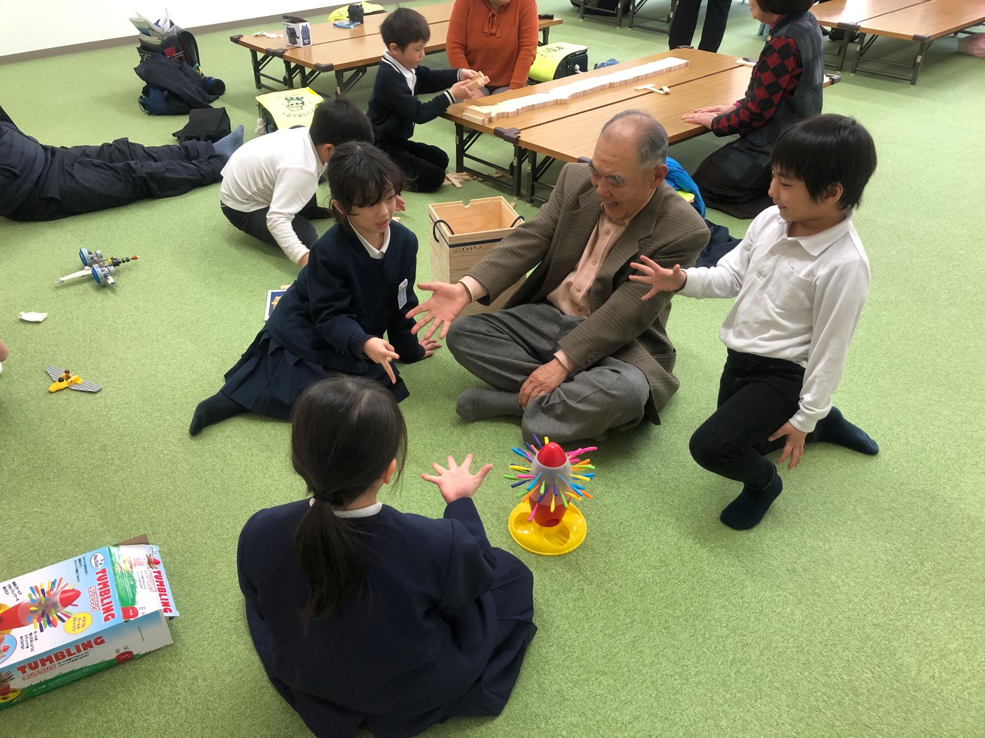 年配の男性と4人の子どもたちが輪になって座り、じゃんけんをしている写真