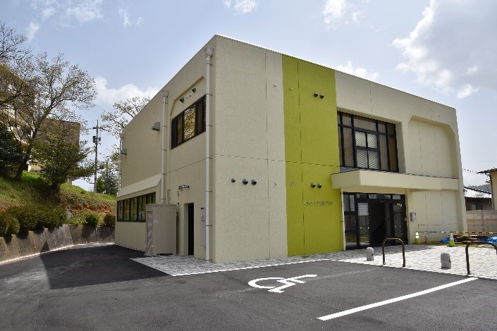 クリーム色に黄緑色で縦の帯状のラインが入った外壁の四角い建物の写真