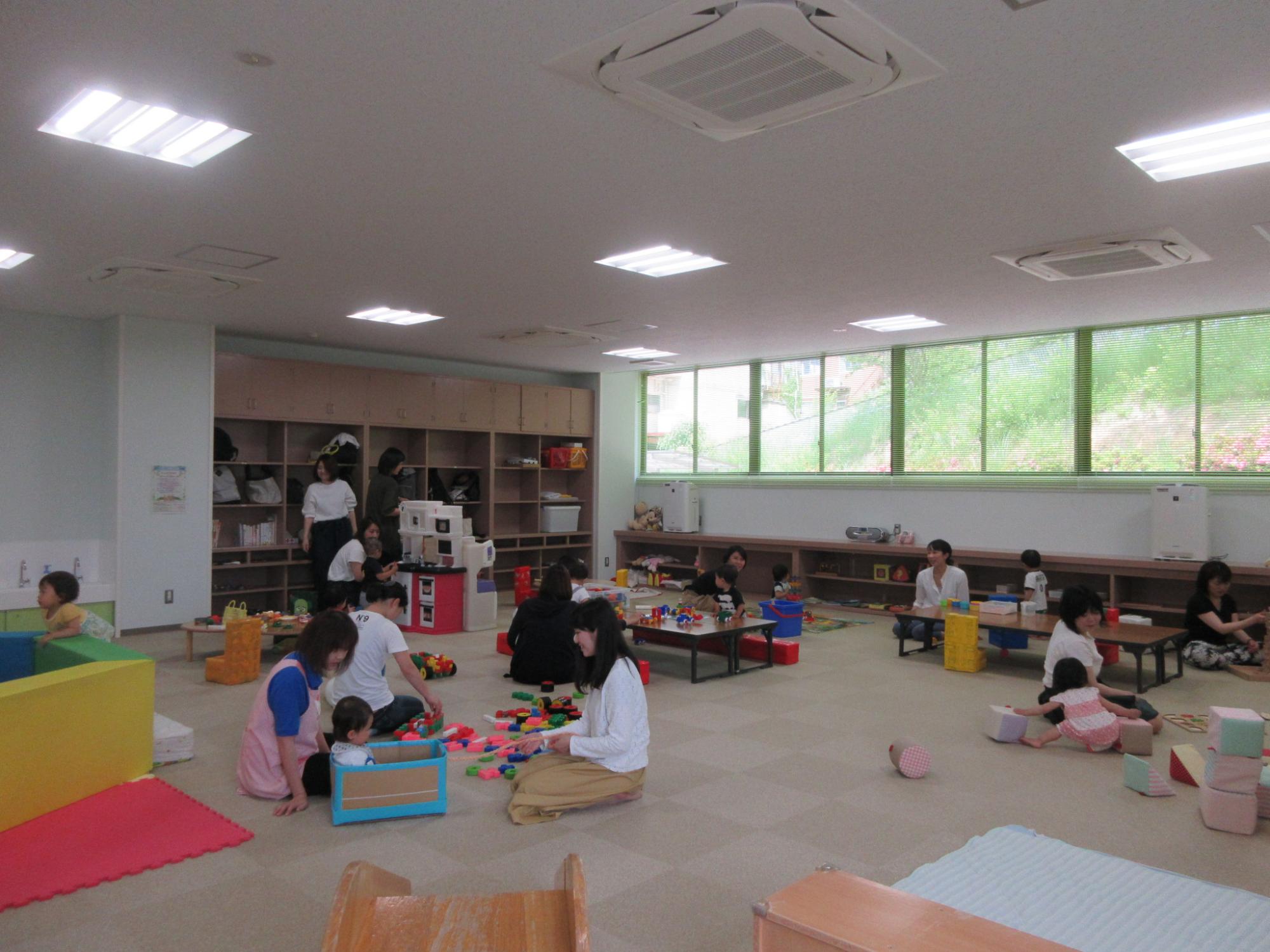 広い室内で複数人の子どもと親がおもちゃを使って一緒に遊んでいる写真