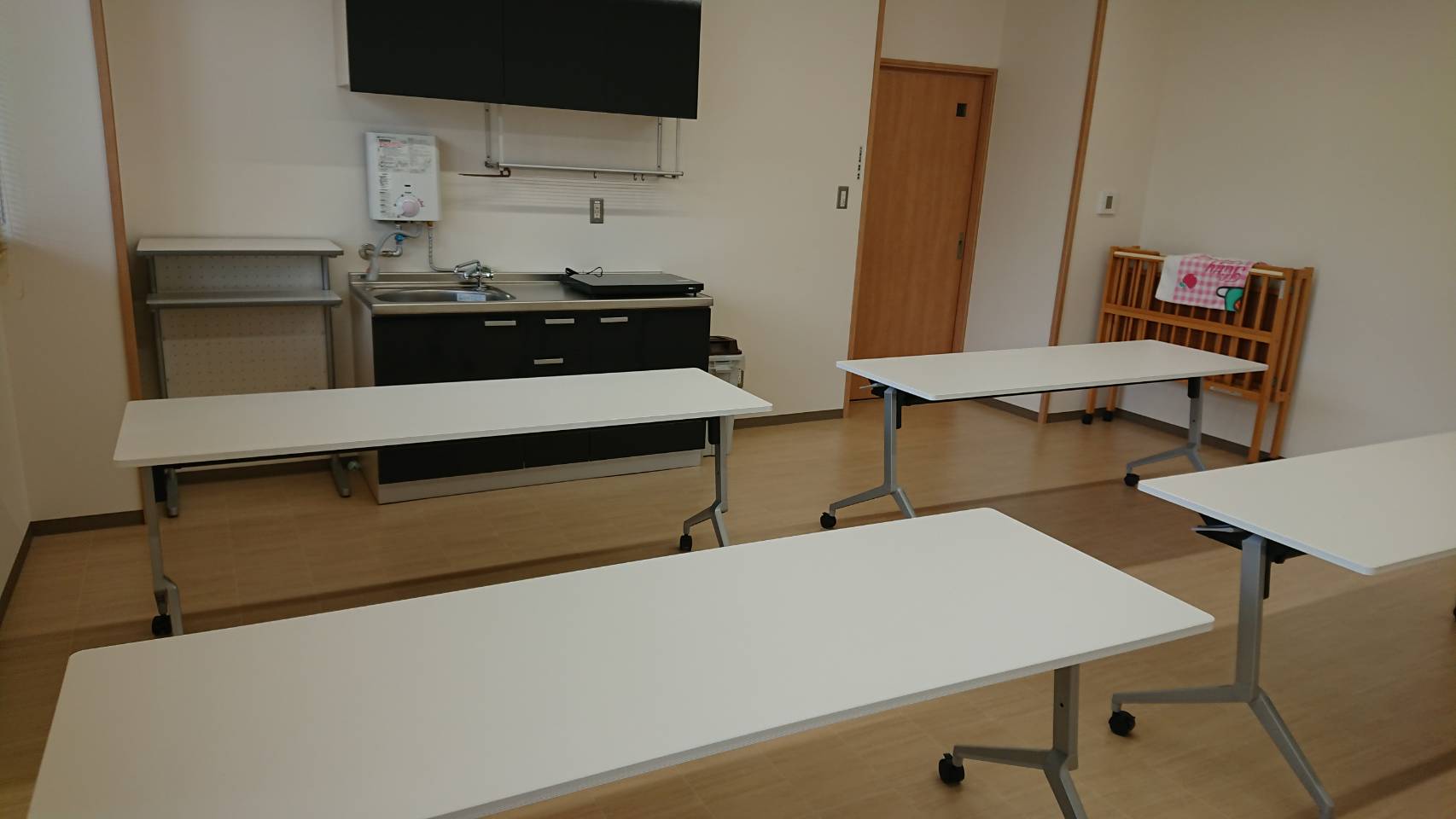 キッチン台が備えられている部屋にテーブルが複数台設置されている室内の写真