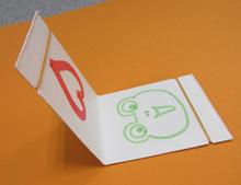 輪ゴムをかけられた白い紙にハートマークとカエルの絵が描かれている写真