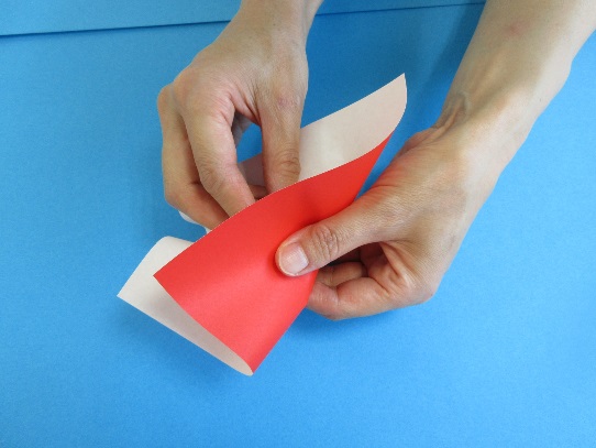 赤い折り紙に力を込めて丸めている写真