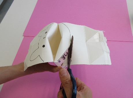 内側に顔の描かれた牛乳パックにハサミを入れている写真