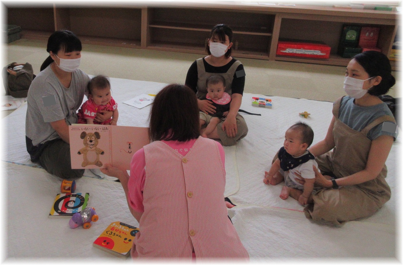 女性が抱っこされた赤ちゃん達に絵本の読み聞かせをしている写真