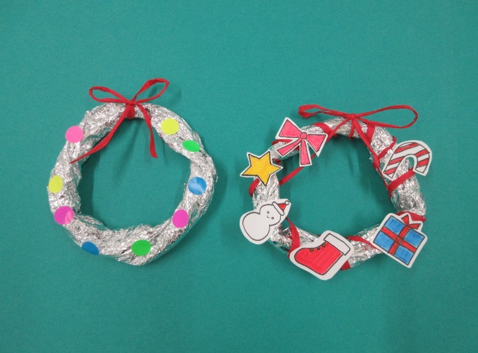 シールで飾り付けられたリースとリボンやプレゼントの箱が描かれた紙で飾り付けられたリースが並べられている写真