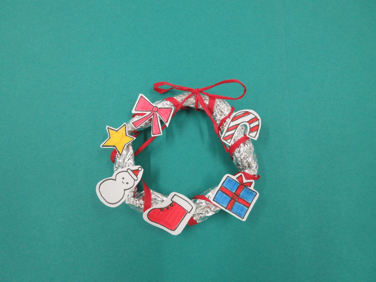 輪っか型のアルミホイルに赤いリボンや星・プレゼントの箱が描かれた紙が付けられている写真