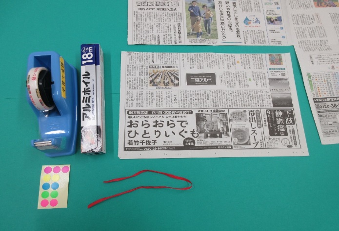 セロテープ、シール、アルミホイル、赤いひも、新聞紙が並んで置かれている写真