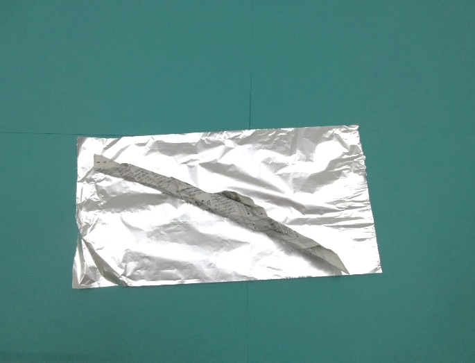 広げられたアルミホイルに棒状の新聞紙が置かれている写真