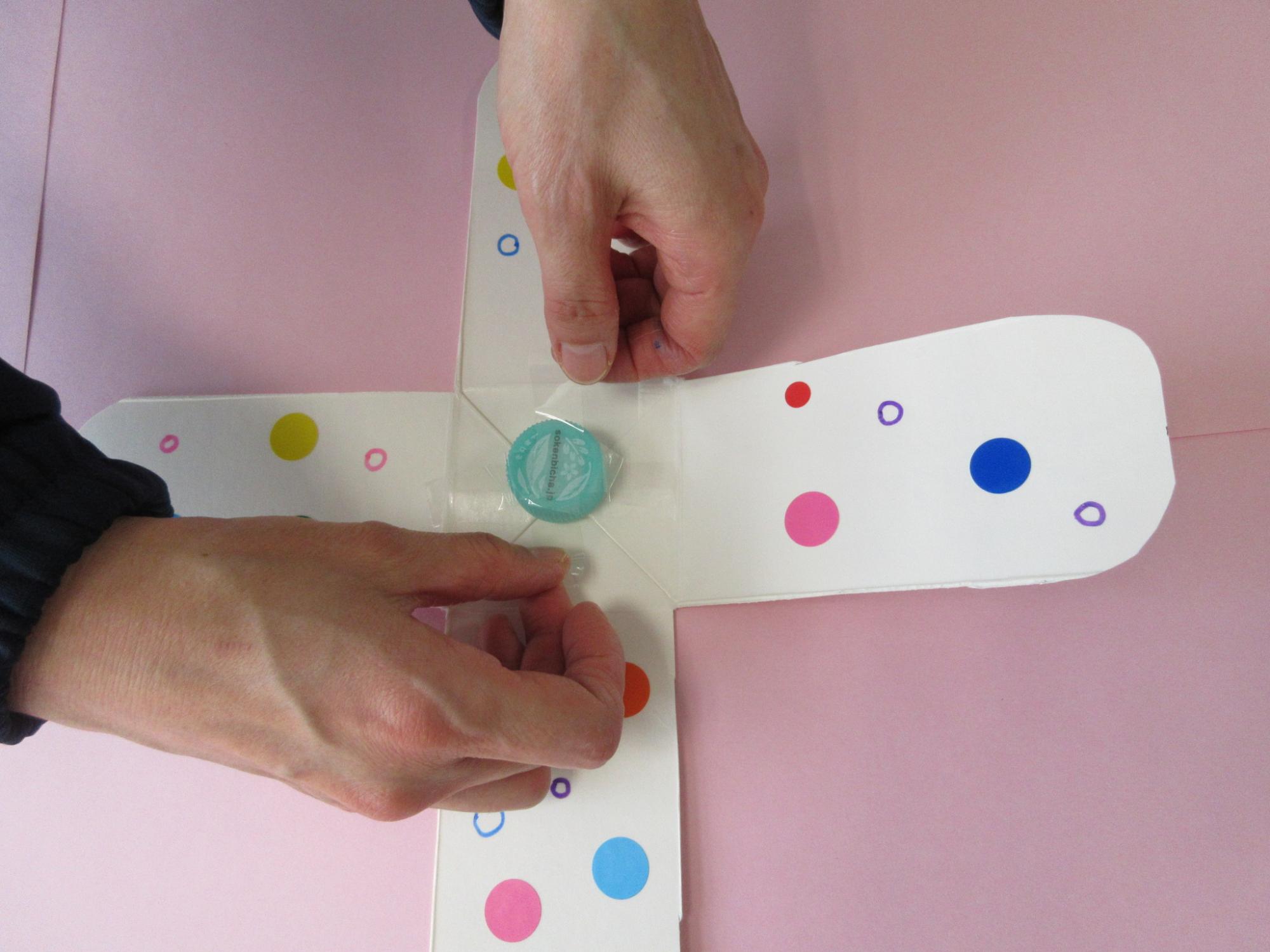 十字に広げられた牛乳パックに水色の丸い物をセロテープで固定している写真