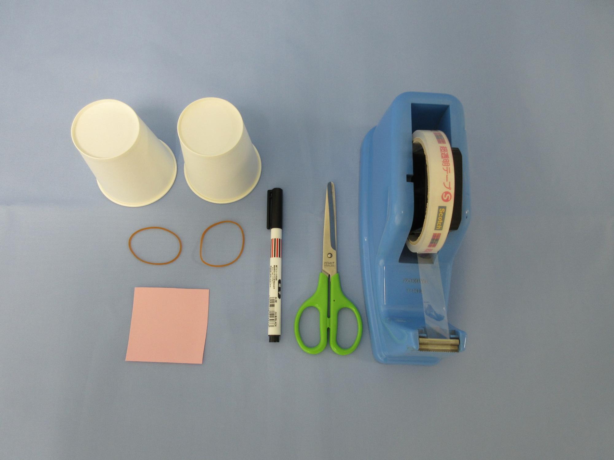 紙コップ、輪ゴム、薄ピンク色の紙、マジック、ハサミ、セロテープが並べて置かれている写真