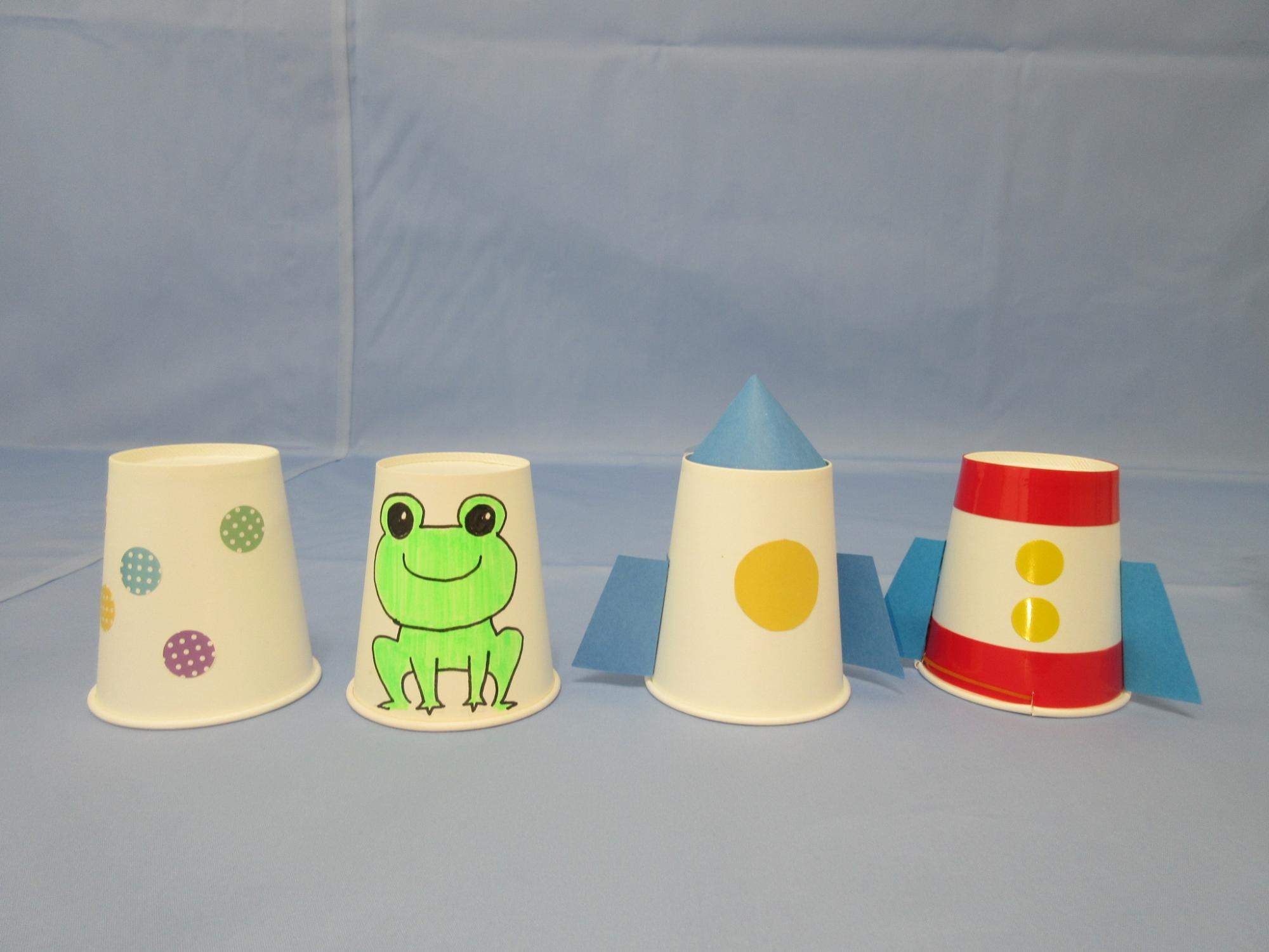 ロケットの飾りが付いた紙コップやカエルの絵が描かれた紙コップなどが並べられている写真