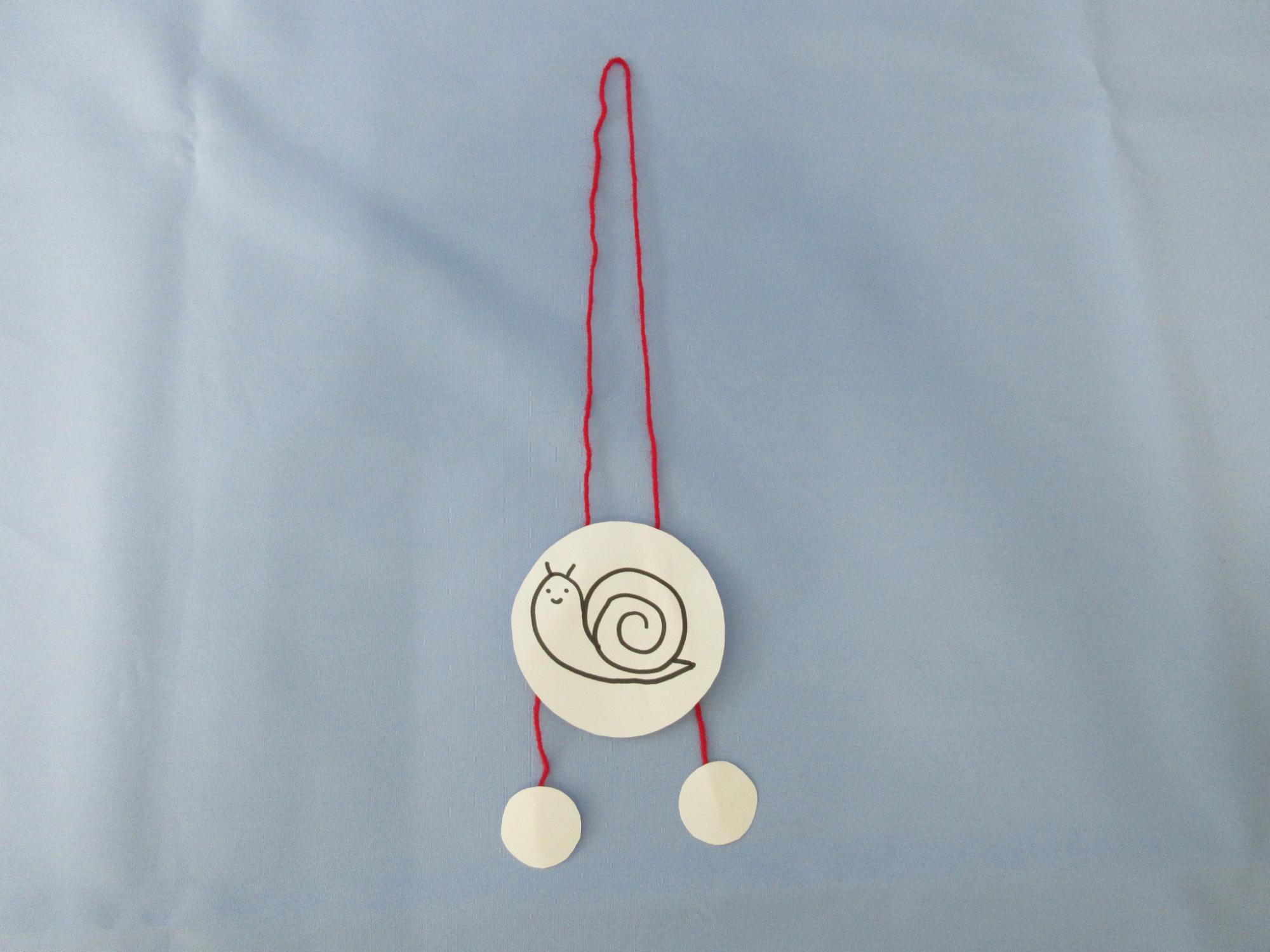 かたつむりが書かれた絵に赤い紐が通されている写真