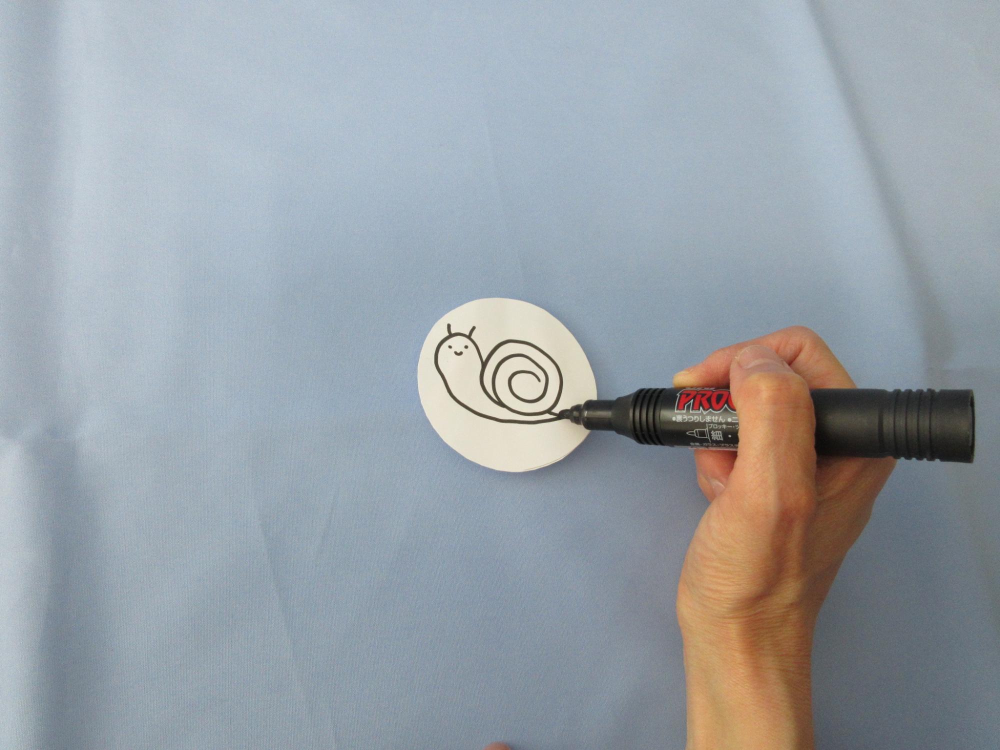 丸い紙にマジックでかたつむりを書いている写真