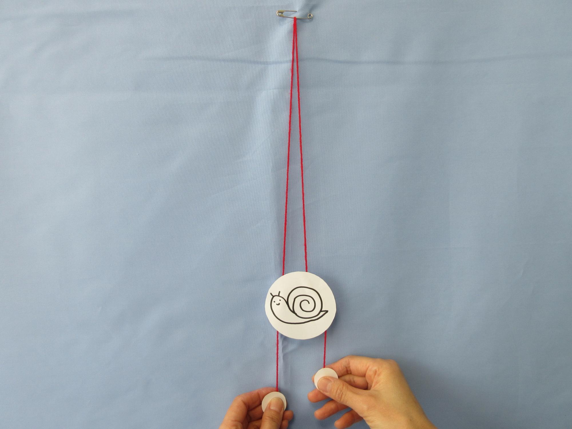 かたつむりの絵が描かれた丸い紙に赤いひもが通されている写真