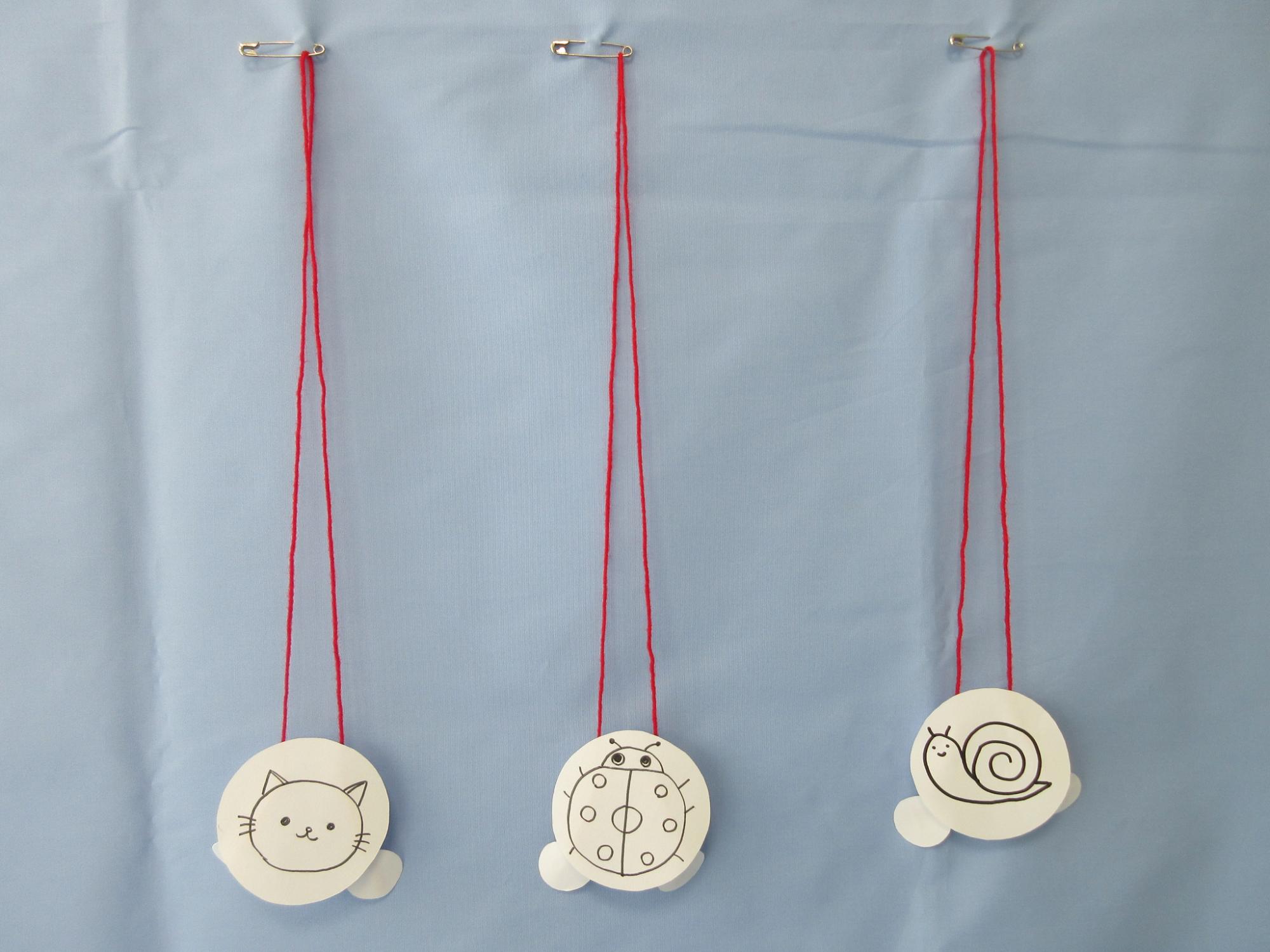 猫、てんとう虫、かたつむりの書かれた丸い紙が赤いひもで安全ピンから吊るされている写真