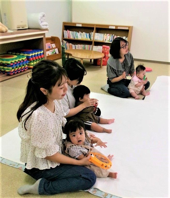 楽器を持って母の膝上でリトミックをしている子どもの様子