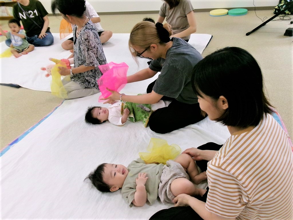 母がカラフルなスカーフで、子どもにいないいないばあーをしている様子