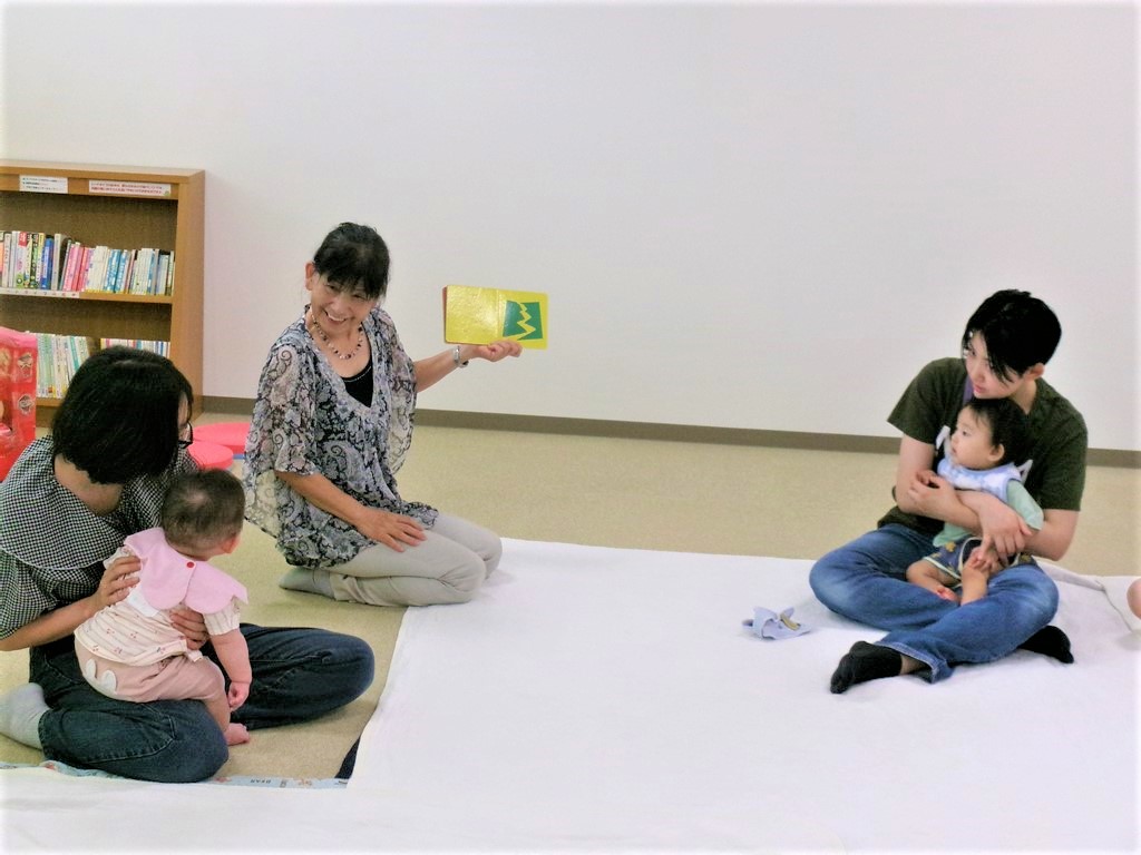 絵本の読み聞かせを母の膝の上で夢中に聞いている子どもの様子