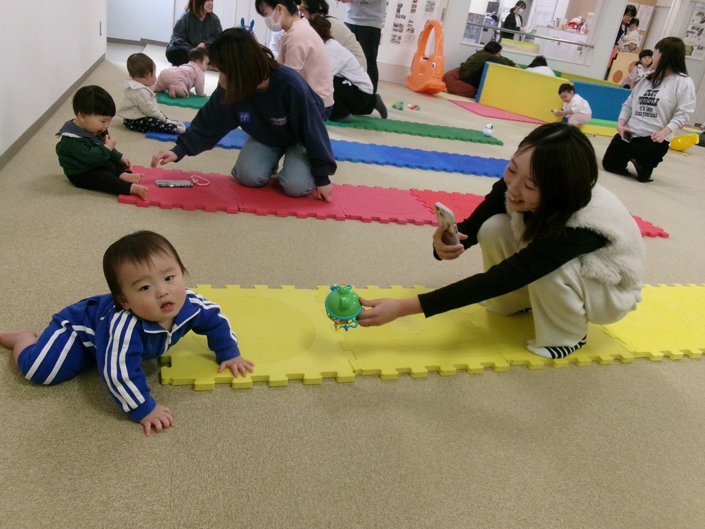 おもちゃを使ってあかちゃんのはいはいを促すお母さんたち