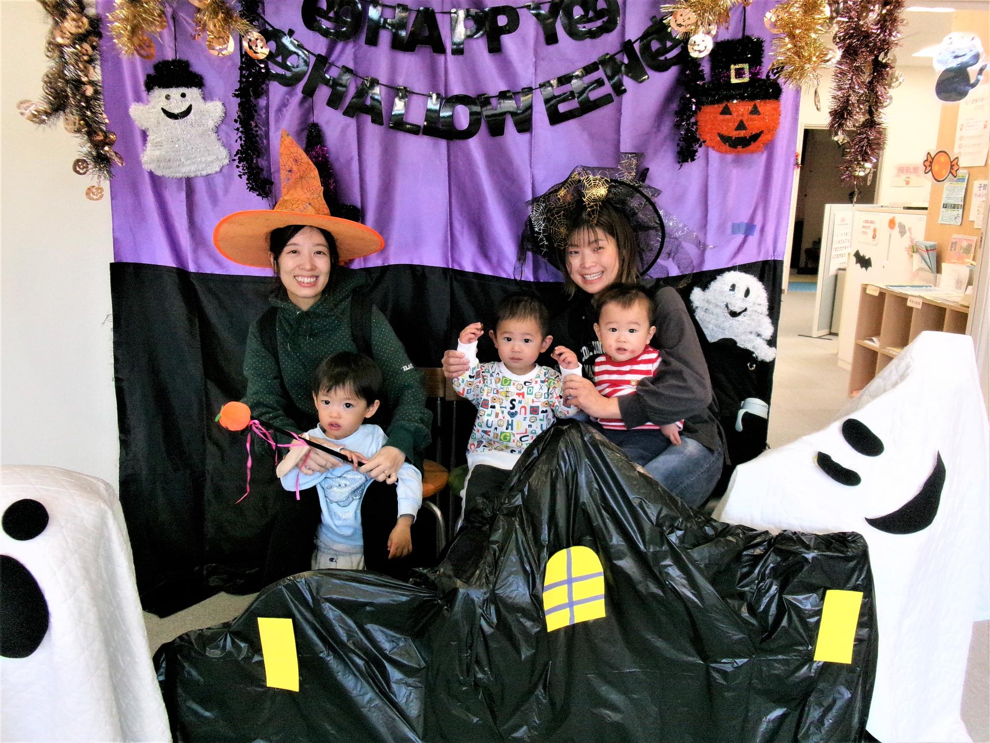ハロウィンフォトコーナーの前で2組の親子が仮装して笑っている写真
