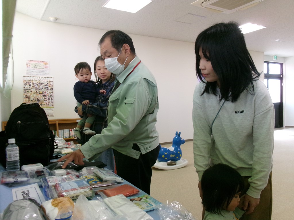 参加者が非常用持出品の展示物について説明を受けている写真