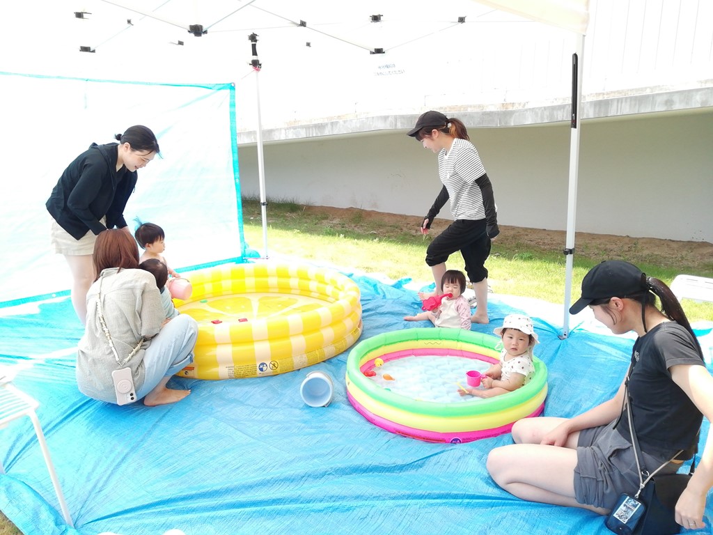 子ども用プールで水遊びをする赤ちゃんとそれを見守る母