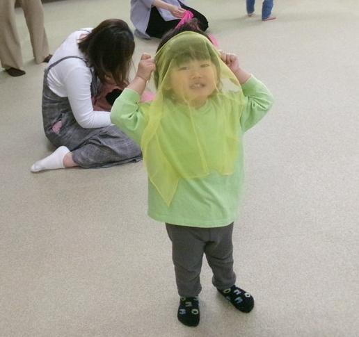 子どもがスカーフで顔を隠し、いないいないばあをしている写真