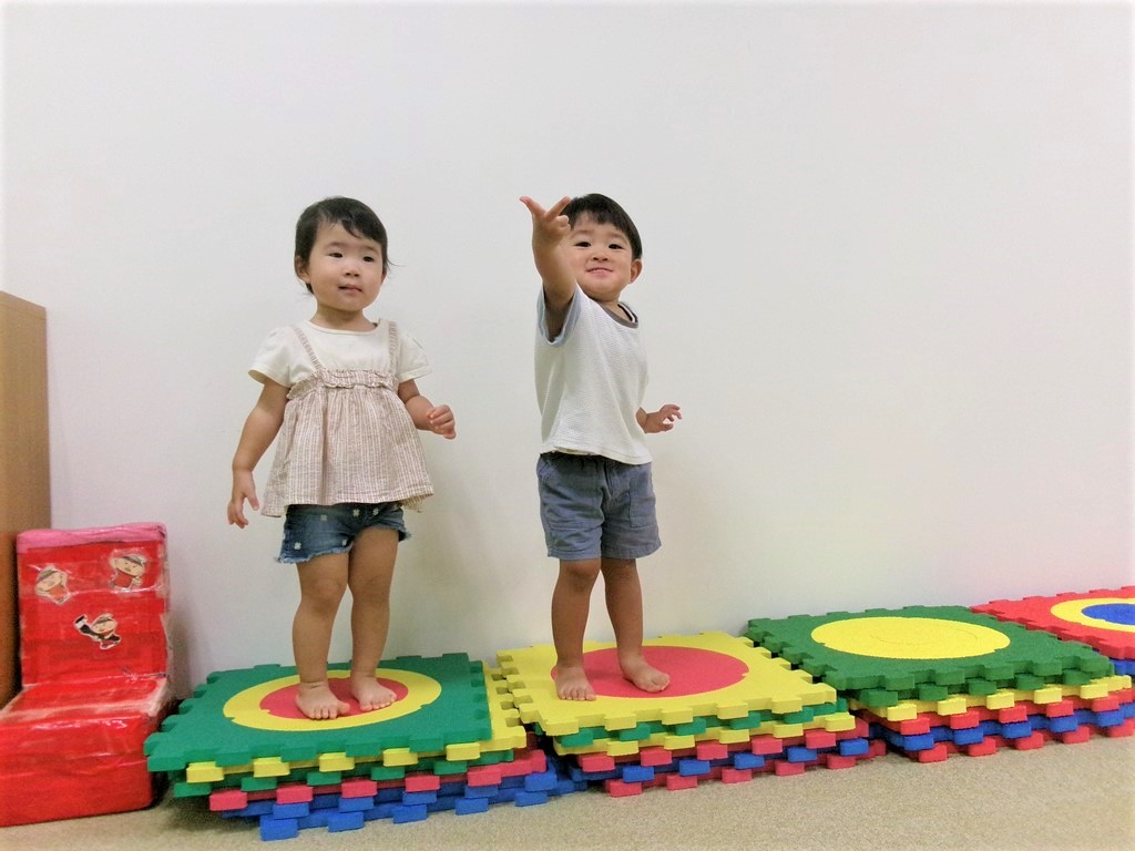 重なったマットの上に立つ女の子とその横でポーズをとる男の子