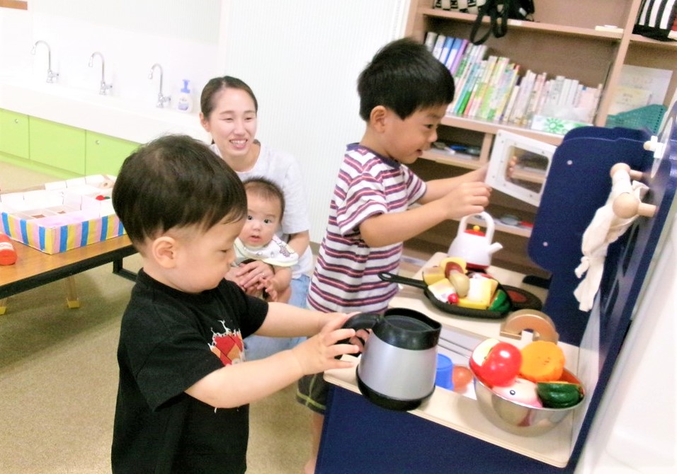 おままごとキッチンで遊ぶ男の子達とその様子を笑顔で見つめる母