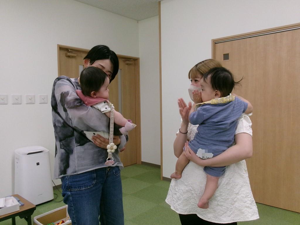女性たちが床のマットに寝かされた赤ちゃんに手で触れている写真