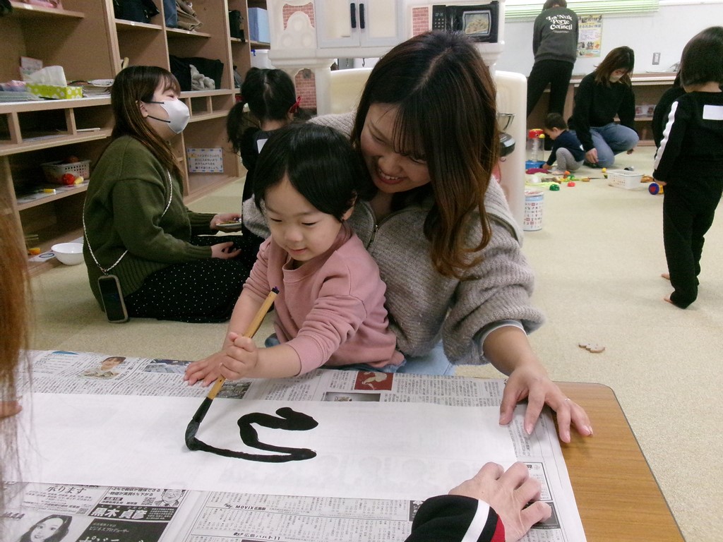 母と一緒に筆を持って書道をする様子