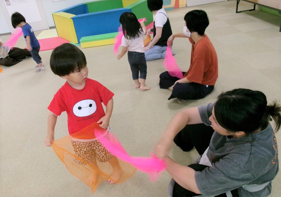 7月わくわくキッズでふわふわスカーフで遊ぶ親子の様子