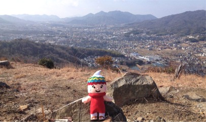 山頂にいるふでりんとその後ろに見渡せる市街地の写真