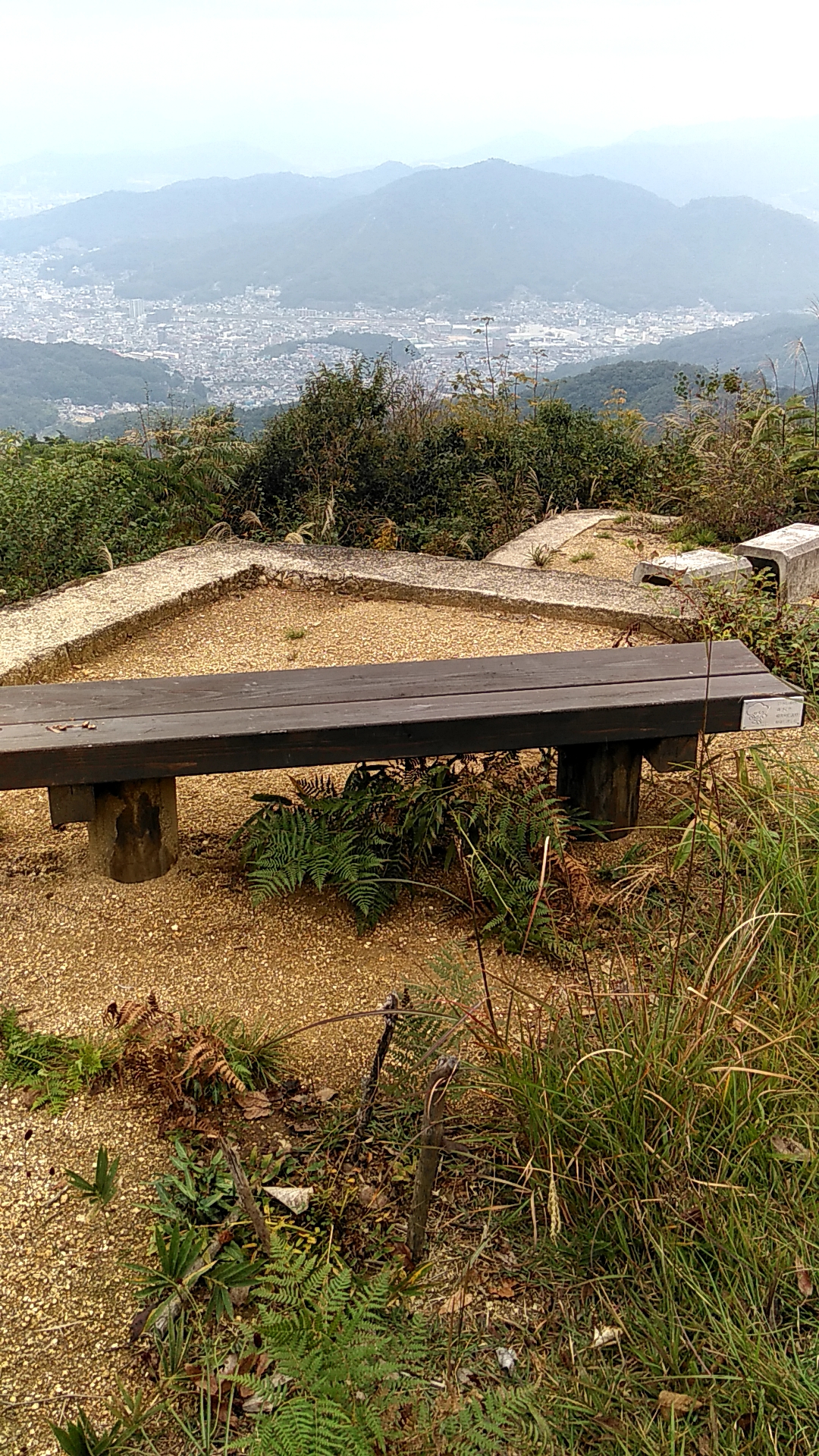 擁壁の上にベンチがあり、そこから市街地や向かいの山を見渡した写真
