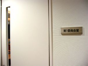 ドアの横に「第1委員会室」と書かれたプレートが飾られている写真