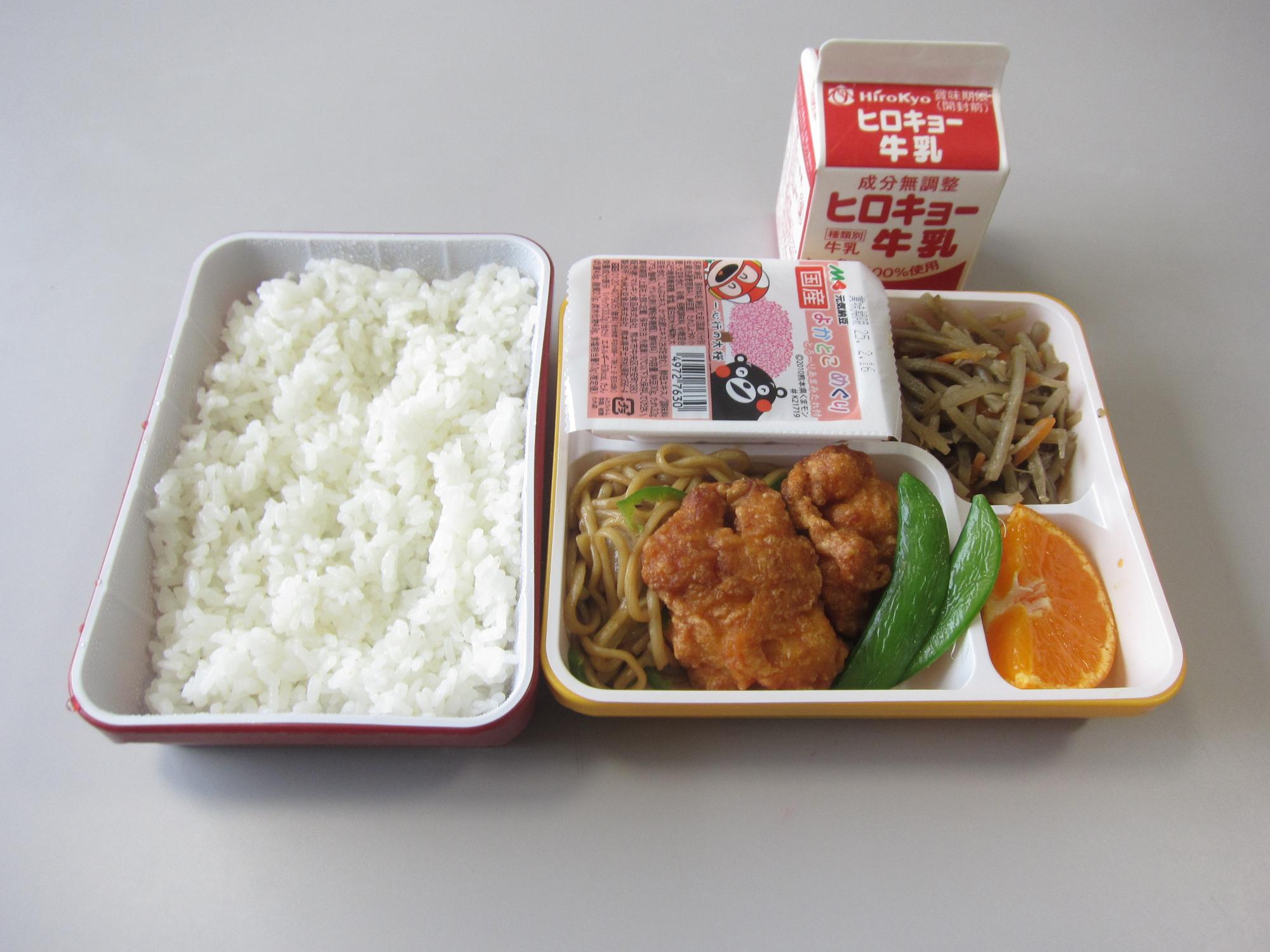 ご飯とおかずが仕切られた弁当箱と牛乳をセットにした学校給食の写真