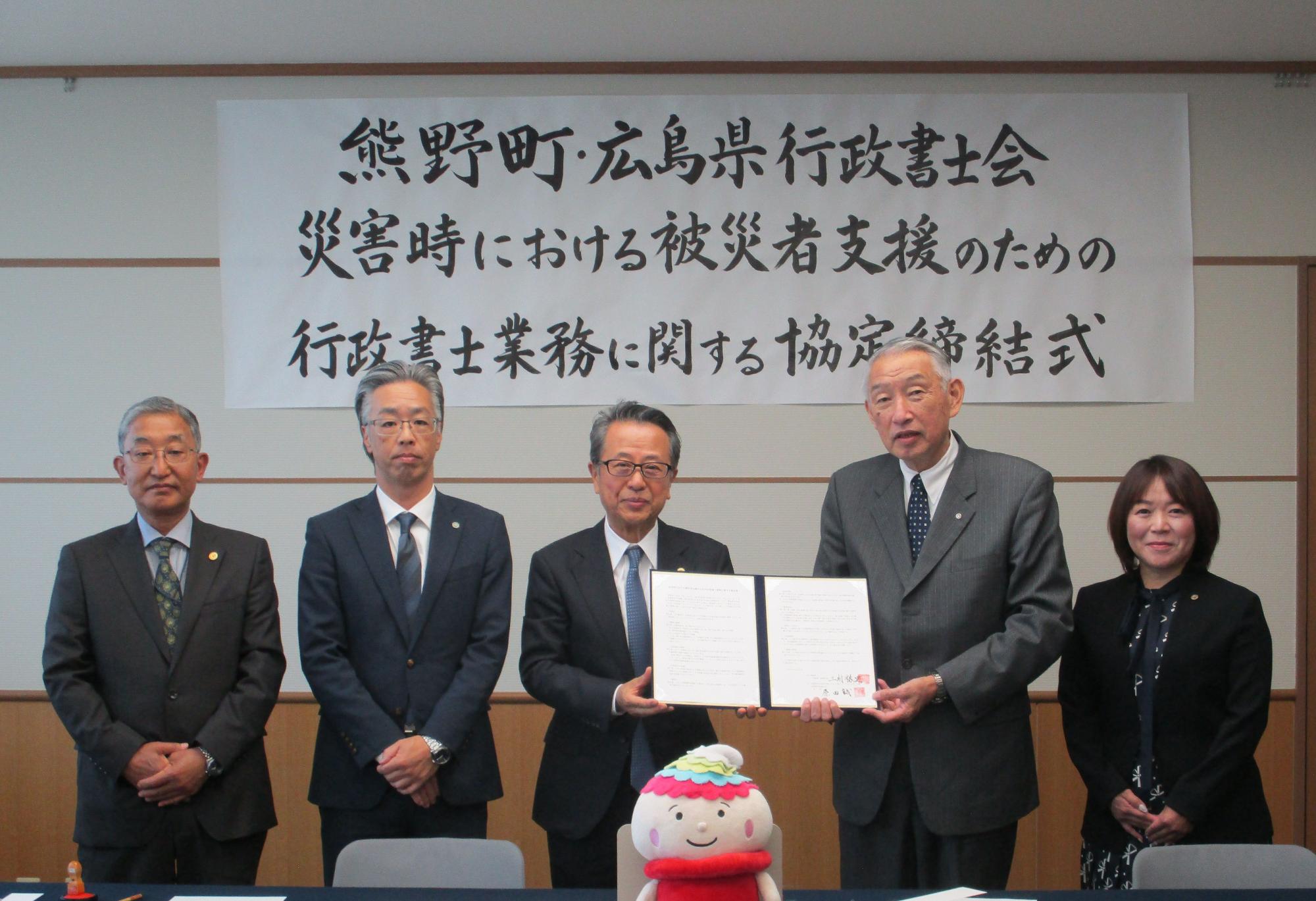 協定締結式で協定書をもちながら記念撮影に臨む熊野町長と行政書士会の方々の写真