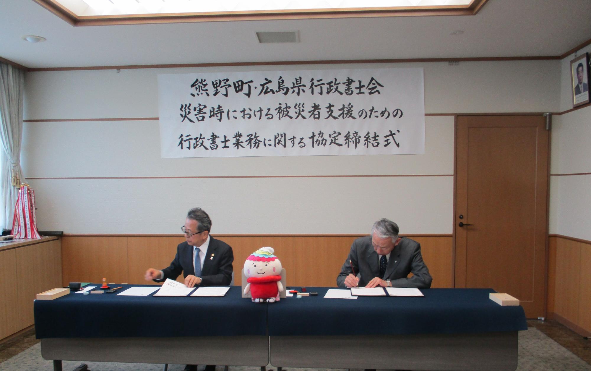協定書にサインをしている熊野町長と行政書士会の方の写真