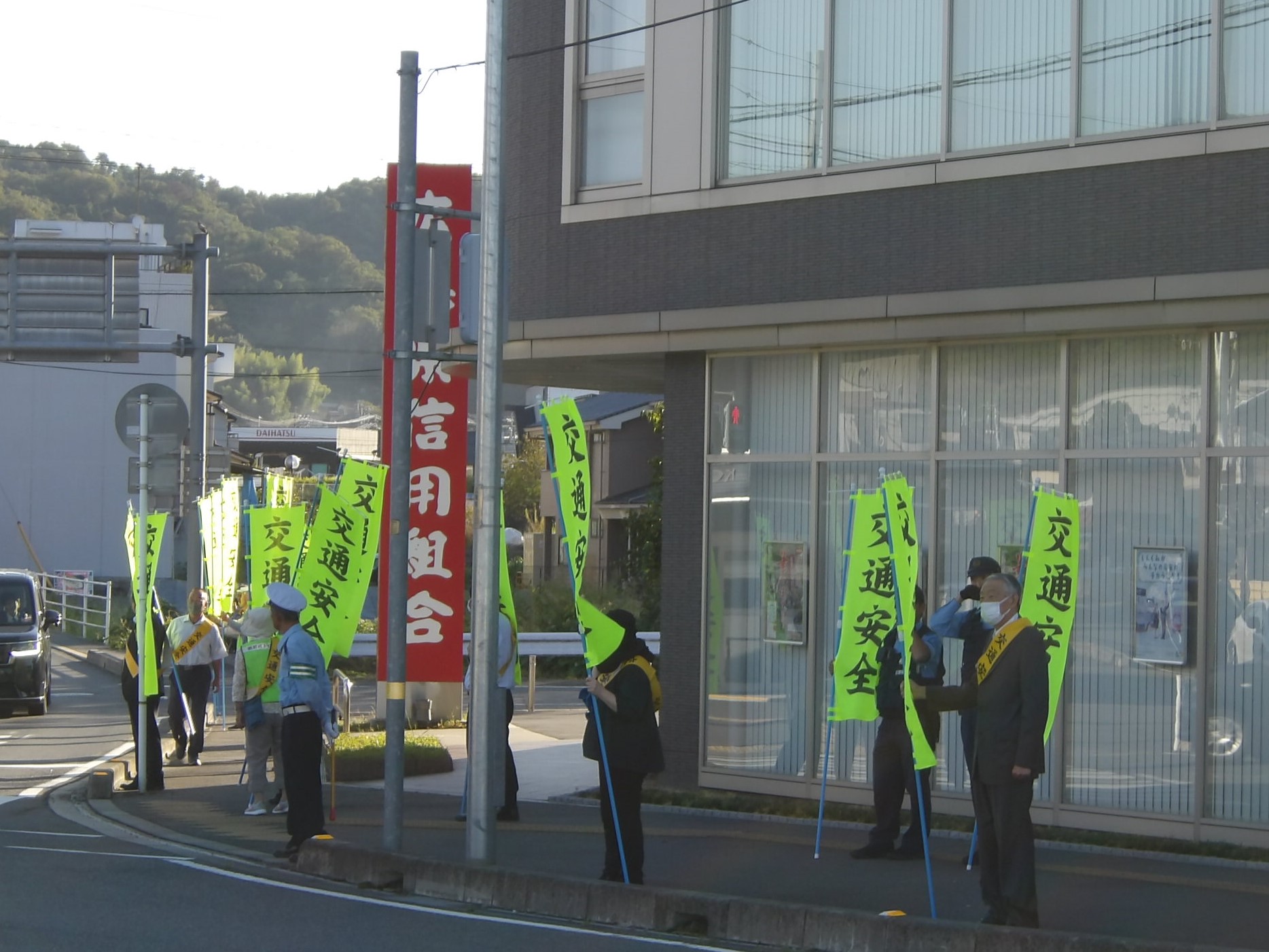 交差点前で緑の交通安全ののぼりを持ちながら見守りをしている警察官の方々の写真