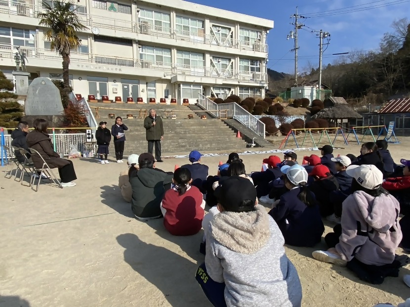 校庭に集まり来賓の挨拶に耳を傾けている小学生たちの写真