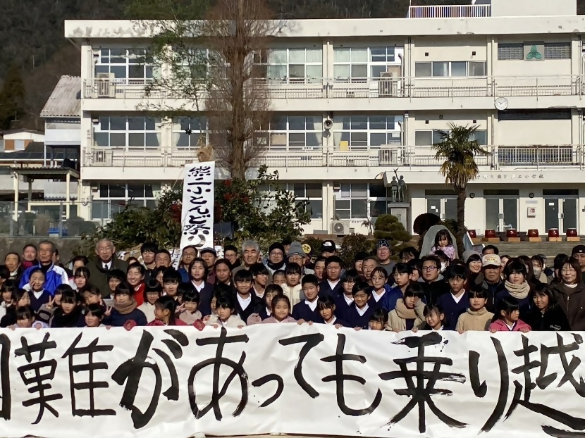 毛筆で手書きされた大きな横断幕を手に持ち記念撮影に臨む小学生たちの写真
