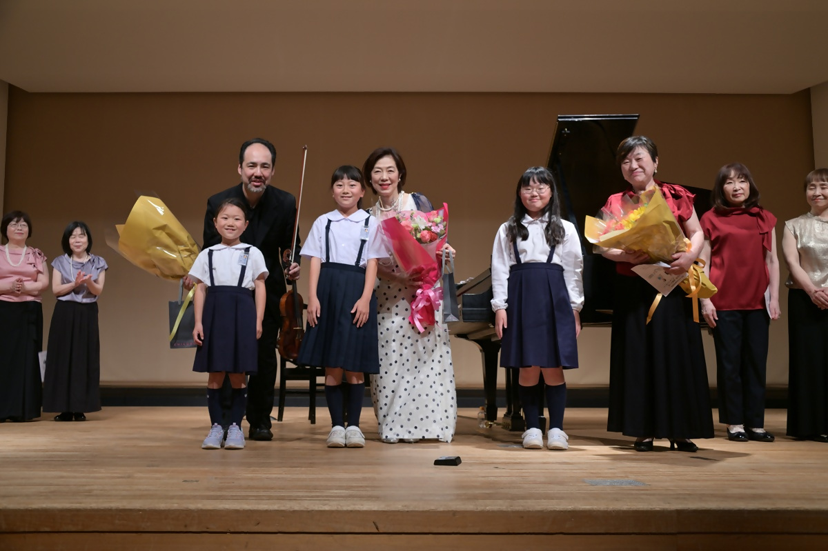 舞台上で花束を贈呈されるヴァイオリン奏者の三又治彦さんとピアニストの遠藤さつきさん、若葉会エレガンスの方々の写真