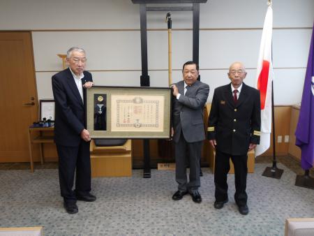 叙勲の症状を掲げて記念撮影に臨む熊野町長と稲垣寿計さんの写真