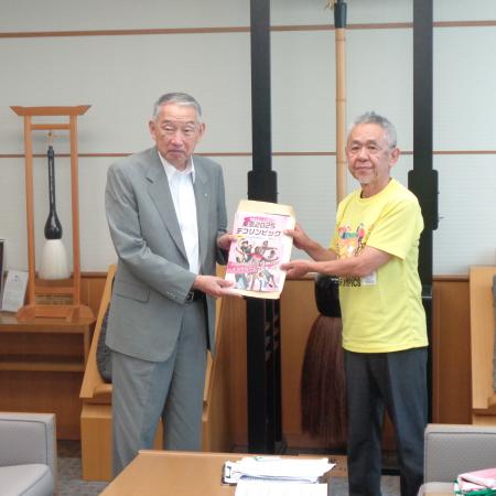 黄色いティーシャツを着た方と一緒にデフリンピックのポスターを持っている熊野町長の写真