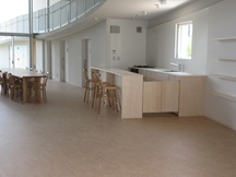 カウンター席があり、机とそれを囲む椅子が置かれている地域カフェの写真