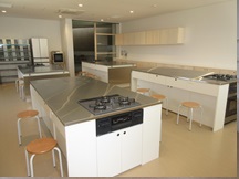 コンロのついた机があり丸椅子が置かれている調理実習室の写真