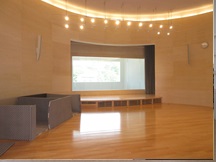 木製の床に橙色の照明、スクリーンがある防災ホールの写真