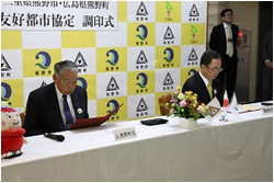 三重県熊野市役所で開催された友好都市協定の調印式で、書類を確認する河上市長と三村町長の写真