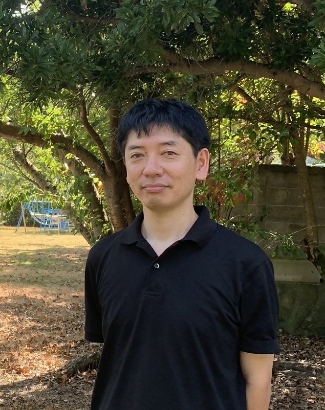 木陰で撮影された黒いポロシャツ姿の田中教授の写真